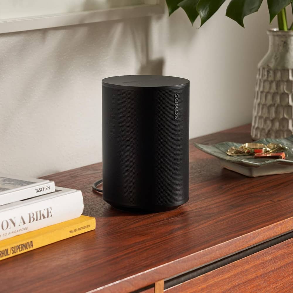 A black Era 100 speaker on a credenza next to books and a vase